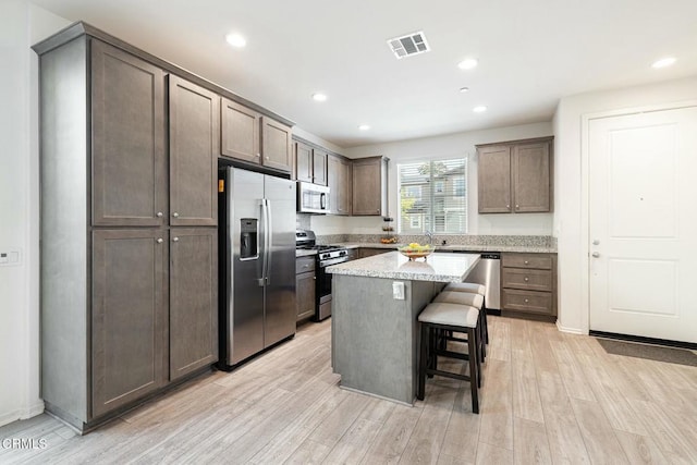 kitchen with visible vents, stainless steel appliances, light wood-style floors, a kitchen breakfast bar, and a center island