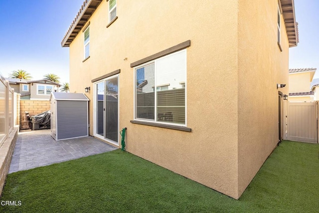 back of house featuring stucco siding, a lawn, a patio, a fenced backyard, and an outdoor structure