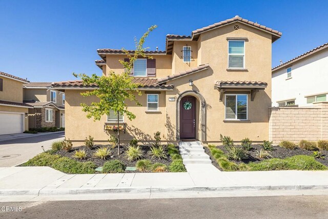 mediterranean / spanish house with a tile roof, fence, and stucco siding