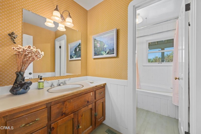 bathroom with vanity, wood finished floors, wallpapered walls, wainscoting, and a washtub