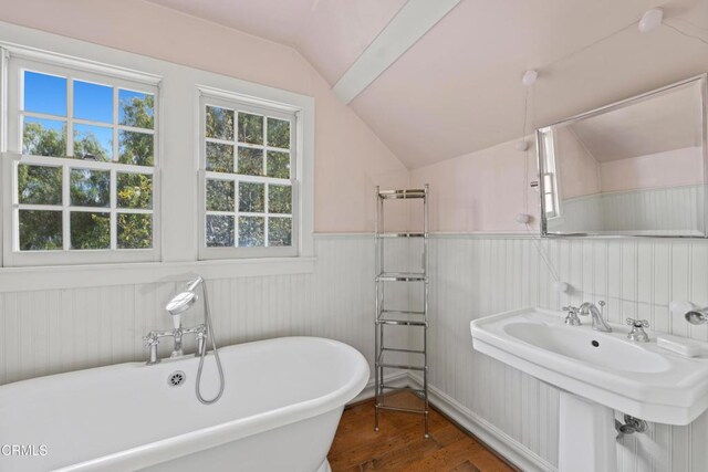 bathroom with wood finished floors, a soaking tub, a sink, vaulted ceiling, and wainscoting