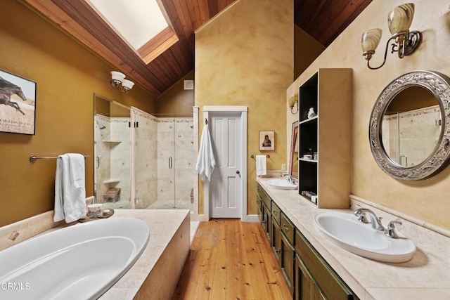 bathroom with a shower stall, vaulted ceiling with skylight, a garden tub, and a sink