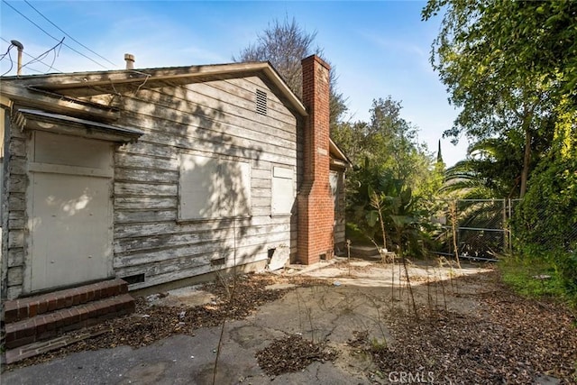 view of property exterior with a chimney, fence, and entry steps