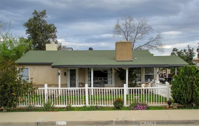 view of front of property with a fenced front yard, stucco siding, a porch, and a chimney