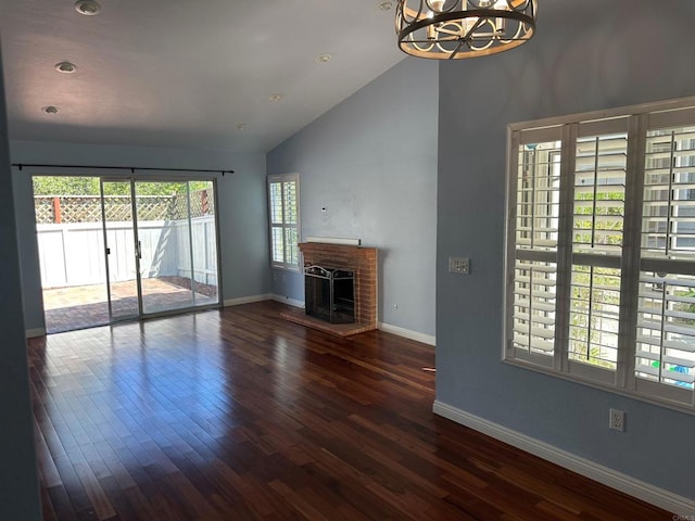 unfurnished living room featuring baseboards, high vaulted ceiling, dark wood-style flooring, a brick fireplace, and a chandelier