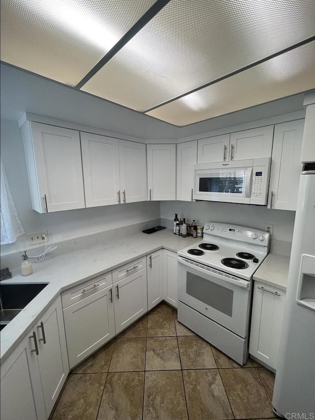 kitchen featuring a sink, white appliances, dark tile patterned flooring, and white cabinets