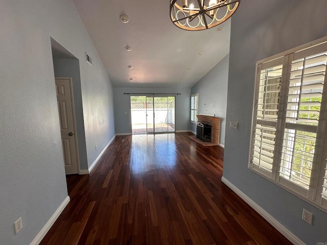 unfurnished living room featuring baseboards, wood finished floors, a brick fireplace, and a chandelier