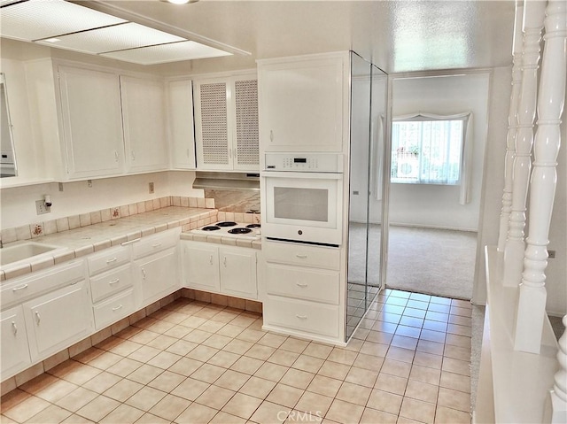 kitchen with tile countertops, light colored carpet, light tile patterned flooring, white appliances, and white cabinetry