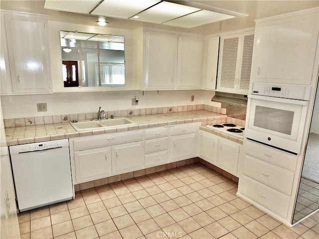 kitchen featuring range hood, light tile patterned flooring, white cabinets, white appliances, and a sink