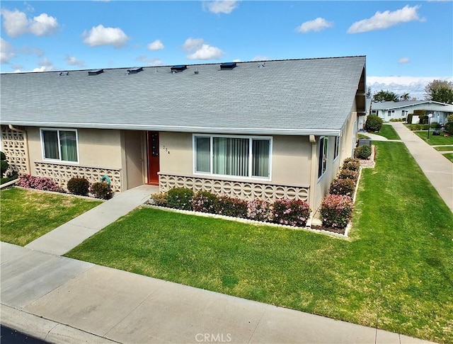 view of front of property with stucco siding, a front yard, and a shingled roof