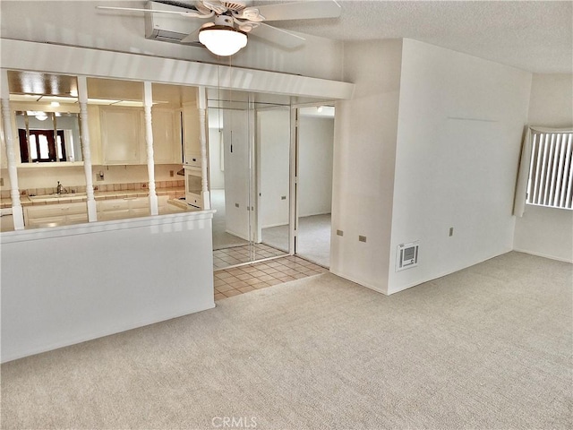 tiled spare room with visible vents, a sink, a textured ceiling, carpet flooring, and ceiling fan