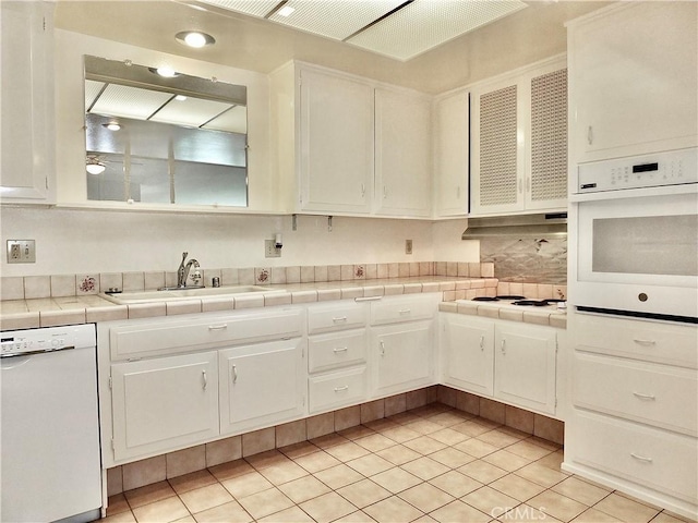 kitchen featuring a sink, white appliances, white cabinets, light tile patterned floors, and tile counters