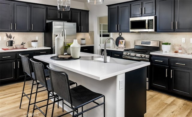 kitchen with stainless steel appliances, a kitchen bar, dark cabinets, and light wood finished floors