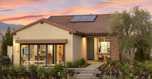 view of front facade featuring solar panels, a tile roof, fence, and stucco siding