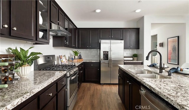 kitchen featuring dark wood-type flooring, a sink, light stone counters, under cabinet range hood, and stainless steel appliances