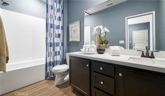 bathroom with visible vents, toilet, shower / bath combo with shower curtain, wood finished floors, and vanity