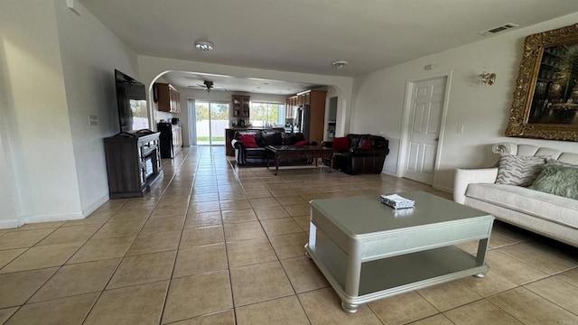 living area featuring light tile patterned floors, a ceiling fan, visible vents, baseboards, and arched walkways