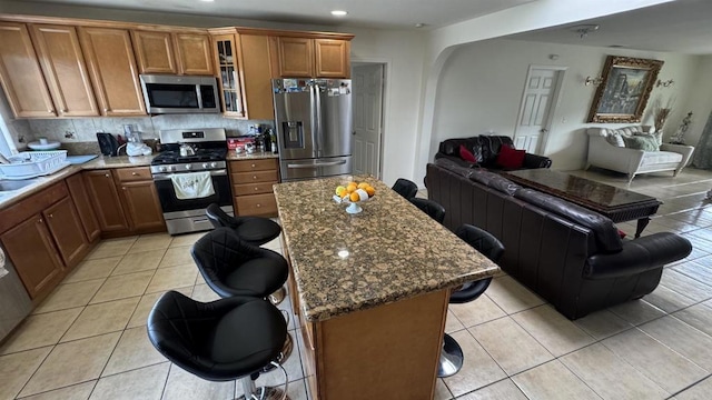 kitchen featuring a kitchen bar, open floor plan, stainless steel appliances, brown cabinetry, and light tile patterned floors