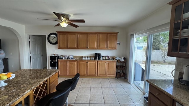 kitchen featuring dark stone countertops, glass insert cabinets, arched walkways, and ceiling fan