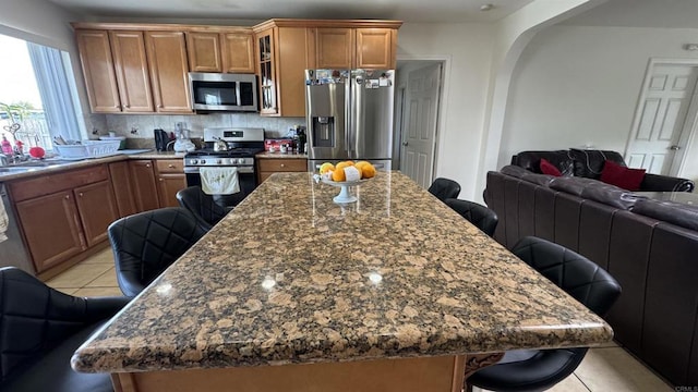 kitchen with open floor plan, a kitchen bar, light tile patterned floors, brown cabinets, and stainless steel appliances