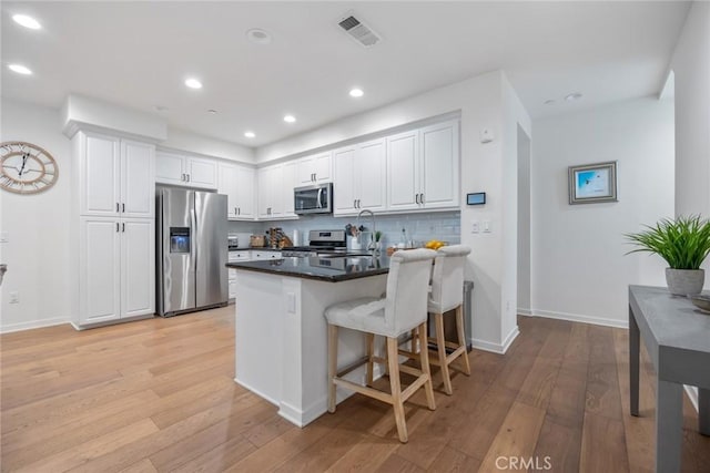 kitchen featuring visible vents, light wood-type flooring, a peninsula, stainless steel appliances, and tasteful backsplash