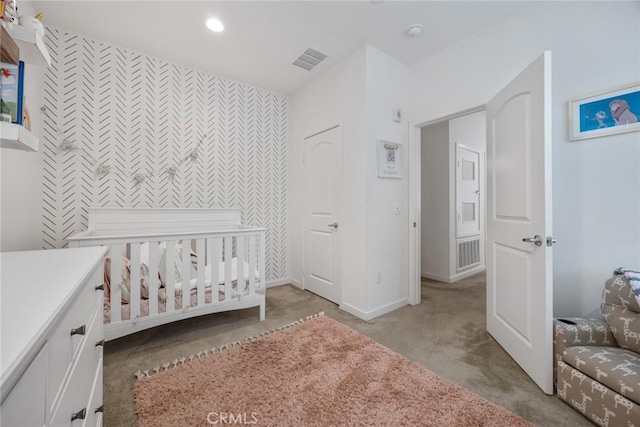 carpeted bedroom featuring visible vents, a nursery area, an accent wall, and baseboards