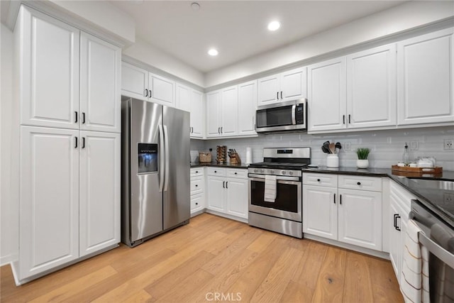 kitchen with dark countertops, white cabinets, appliances with stainless steel finishes, and light wood-type flooring