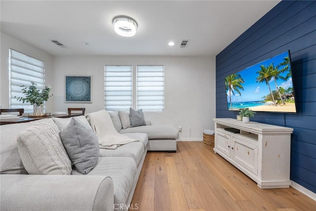 living area featuring light wood-style floors, visible vents, wood walls, and baseboards