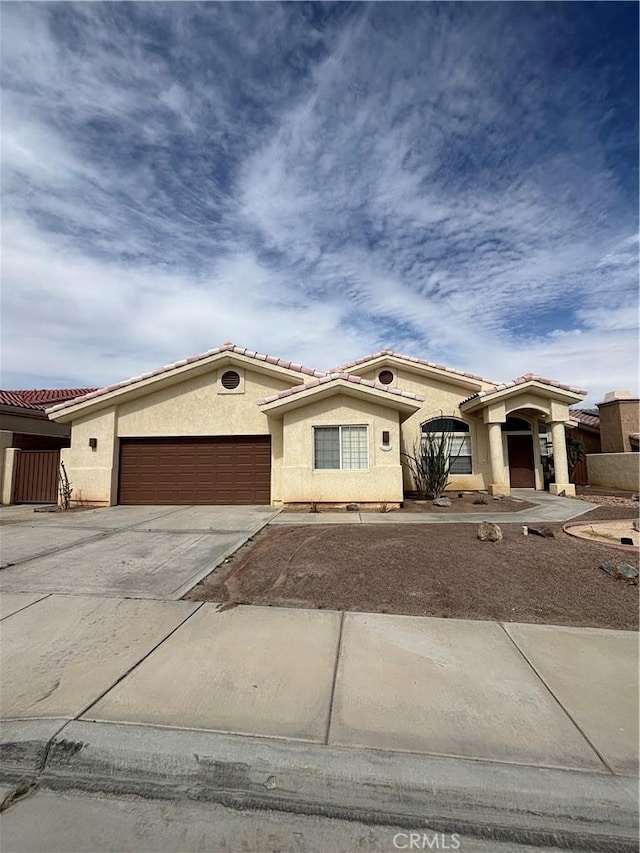 mediterranean / spanish house with concrete driveway, an attached garage, a tile roof, and stucco siding