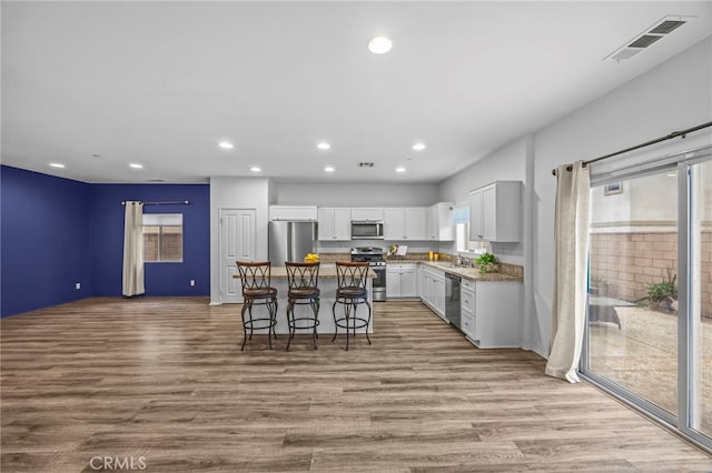 kitchen with light wood-type flooring, a center island, appliances with stainless steel finishes, and visible vents