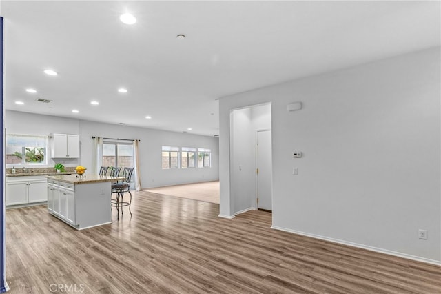 kitchen with white cabinets, a kitchen bar, light wood-style floors, open floor plan, and a center island