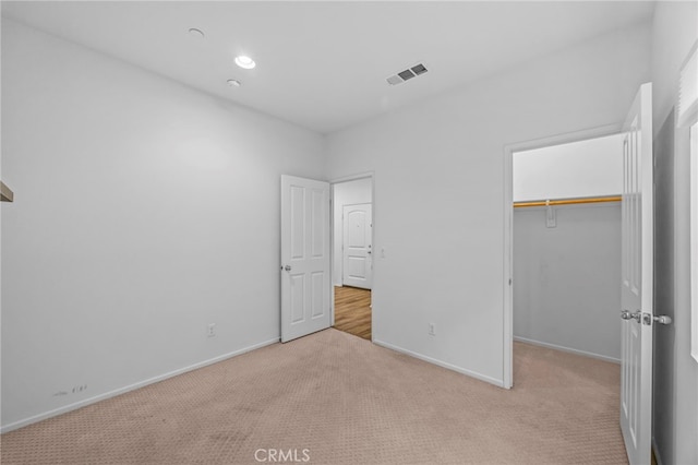 unfurnished bedroom featuring a spacious closet, carpet floors, baseboards, and visible vents