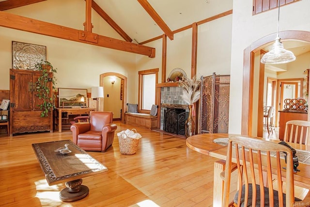 living room with high vaulted ceiling, beam ceiling, arched walkways, wood-type flooring, and a tiled fireplace