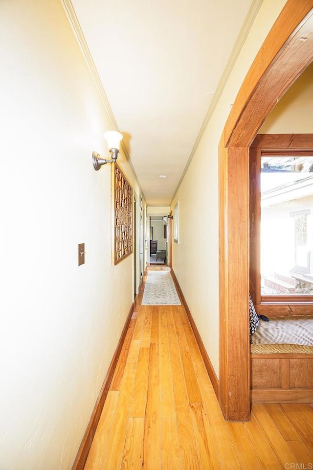 hall with light wood finished floors, crown molding, and baseboards