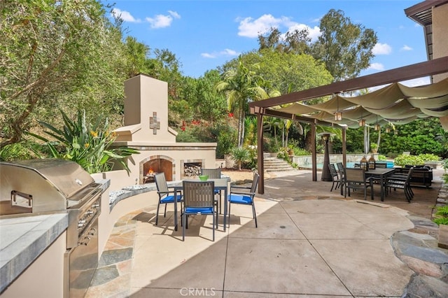 view of patio with an outdoor kitchen, a warm lit fireplace, outdoor dining space, and a grill