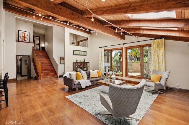 living area with track lighting, stairway, beamed ceiling, a skylight, and wood finished floors