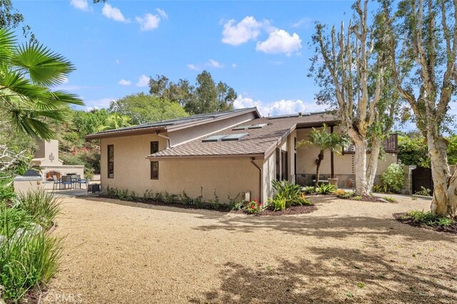 view of side of property with a patio, stucco siding, and a shingled roof