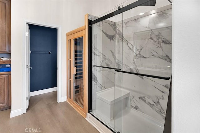 full bathroom with a marble finish shower, baseboards, and wood finished floors