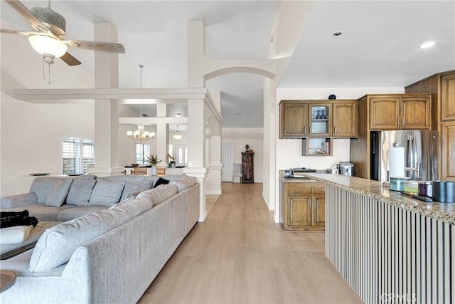 kitchen with glass insert cabinets, light wood-style flooring, arched walkways, freestanding refrigerator, and brown cabinetry