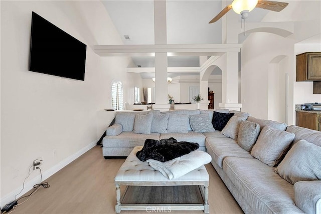 living area featuring light wood-type flooring, beam ceiling, arched walkways, baseboards, and ceiling fan