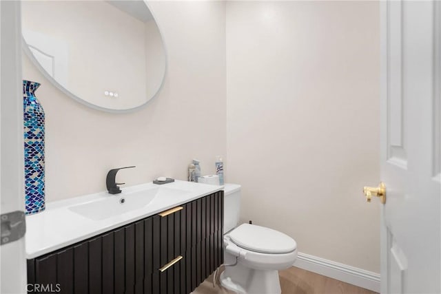 half bath featuring baseboards, toilet, wood finished floors, and vanity