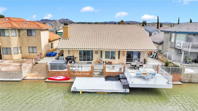 rear view of property with a water view, a tile roof, stucco siding, a chimney, and a patio area