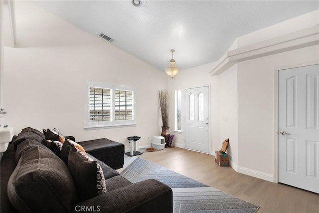 living room with vaulted ceiling, light wood-style floors, visible vents, and baseboards