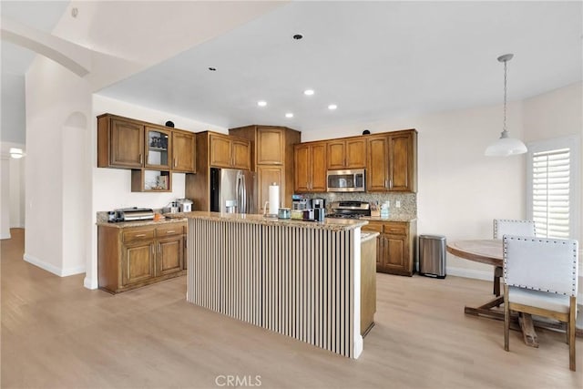 kitchen featuring glass insert cabinets, decorative backsplash, brown cabinets, arched walkways, and stainless steel appliances