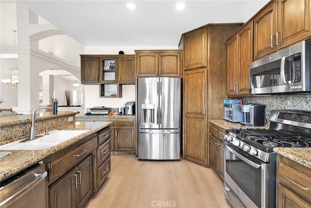 kitchen featuring light stone countertops, appliances with stainless steel finishes, light wood-style floors, arched walkways, and a sink