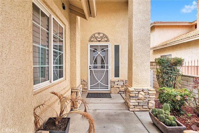 entrance to property featuring stone siding, stucco siding, and fence