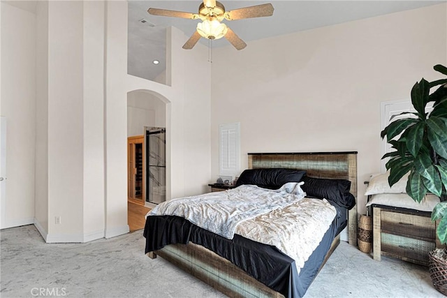 carpeted bedroom featuring ceiling fan, baseboards, arched walkways, and a towering ceiling