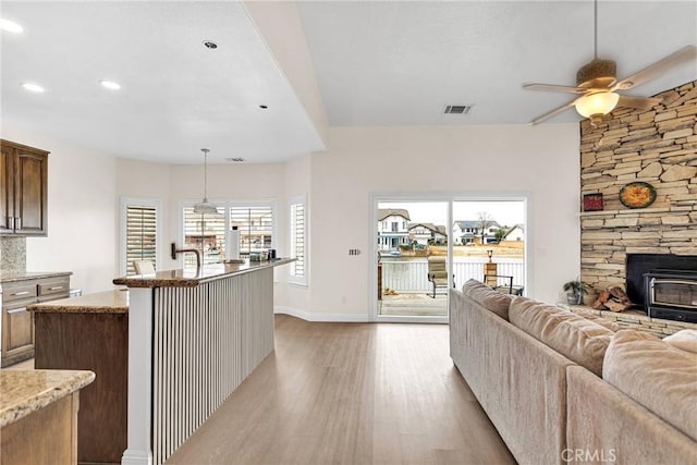 kitchen with a center island with sink, open floor plan, light wood-style floors, light stone countertops, and ceiling fan