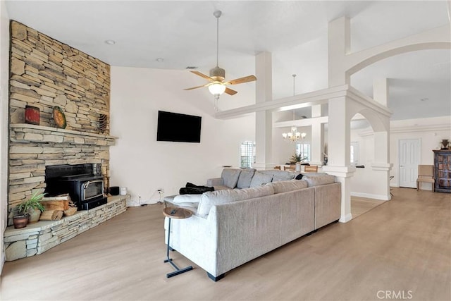 living area featuring ceiling fan with notable chandelier, a wood stove, light wood-style floors, and arched walkways