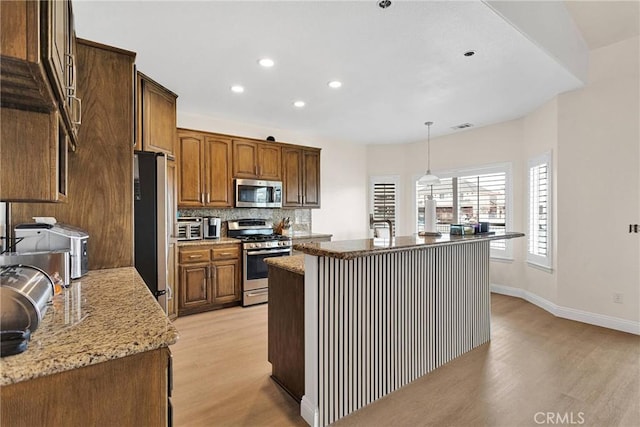 kitchen with visible vents, a kitchen island with sink, light wood-style flooring, backsplash, and appliances with stainless steel finishes